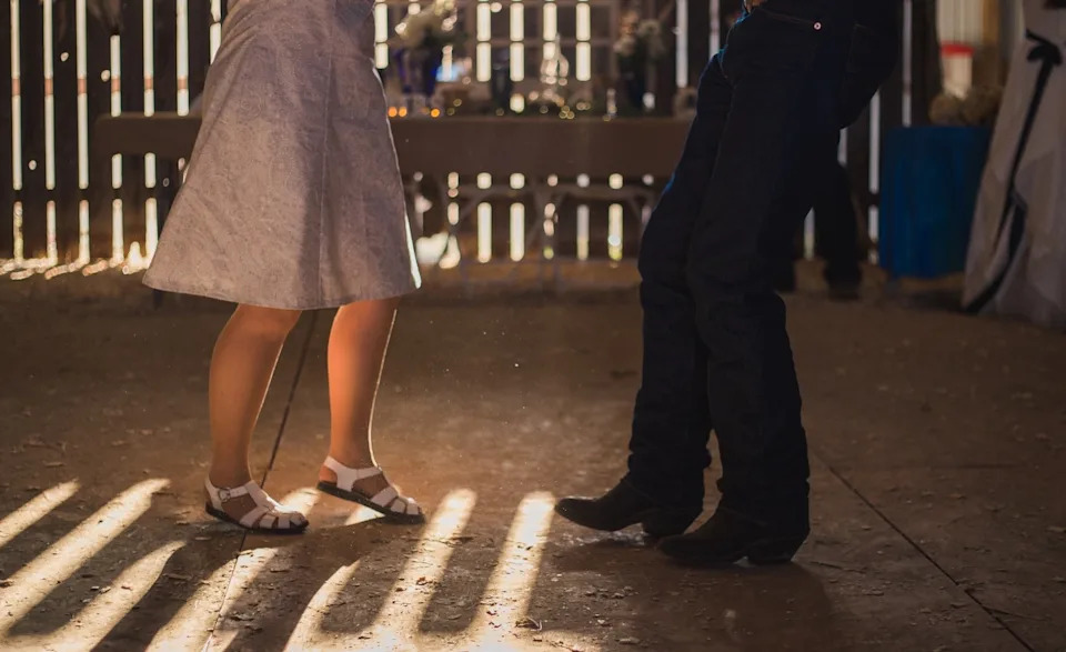 Two people dance on a wooden floor in a sunlit room, casting long shadows