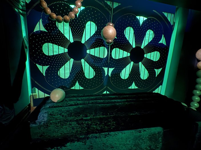 A room lit in green with oversized pearls dangling from the ceiling and velvet upholstery