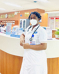 A woman in a doctor's coat with a stethescope around her neck and wearing a white mask leans against a counter.