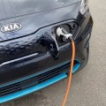 An orange charging cable is plugged into the front of a dark blue Kia.