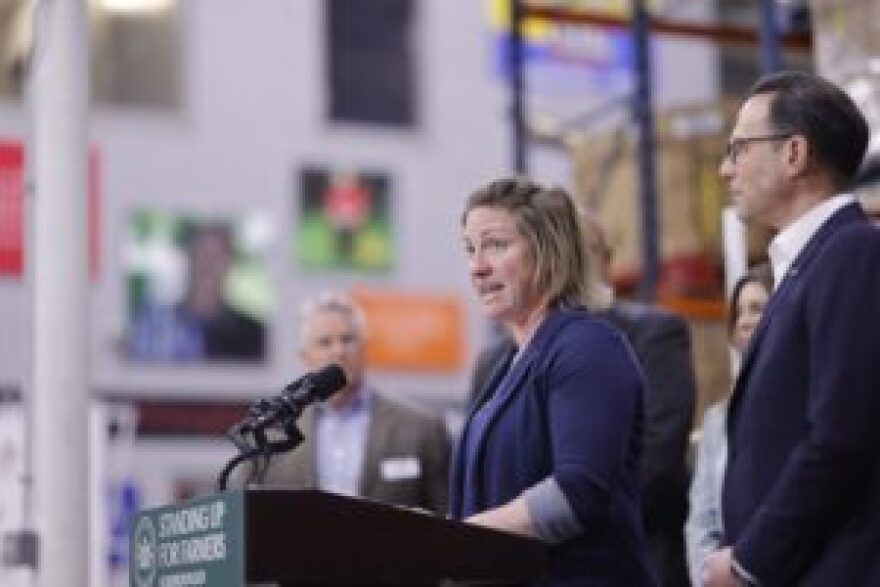 Amy Brickner, a blonde woman wearing a blue blazer, speaks at a podium.