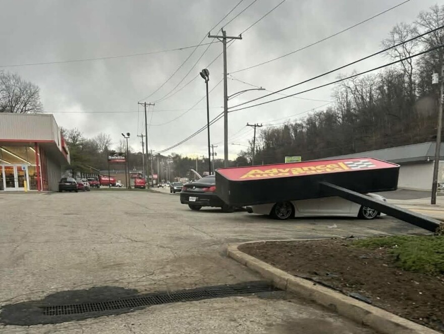 A large sign lies atop a car after falling on it in a parking lot