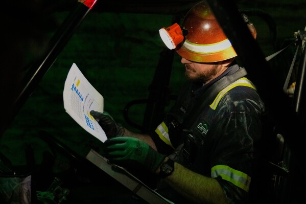 The absolute darkness of the mine is broken as supervisor Andrew Adkins uses a headlamp to lookover a map of drilling sites at the Cargill Salt Mine, 1,800 feet below the surface of Lake Erie, in Cleveland, Ohio, Thursday, March 19, 2026. (AP Photo/Sue Ogrocki)