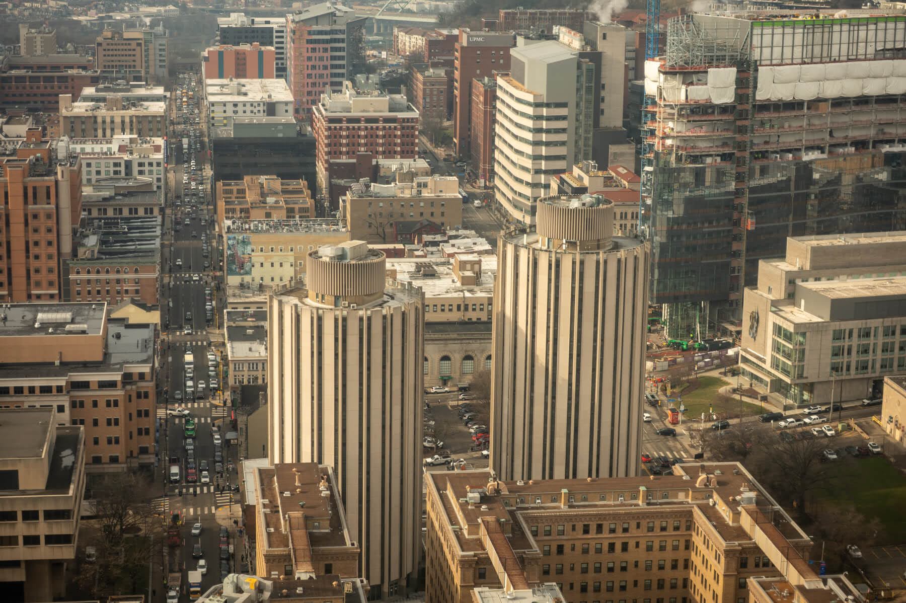 Aerial view of a cityscape featuring two tall, cylindrical buildings with vertical stripes, surrounded by various office and residential buildings.