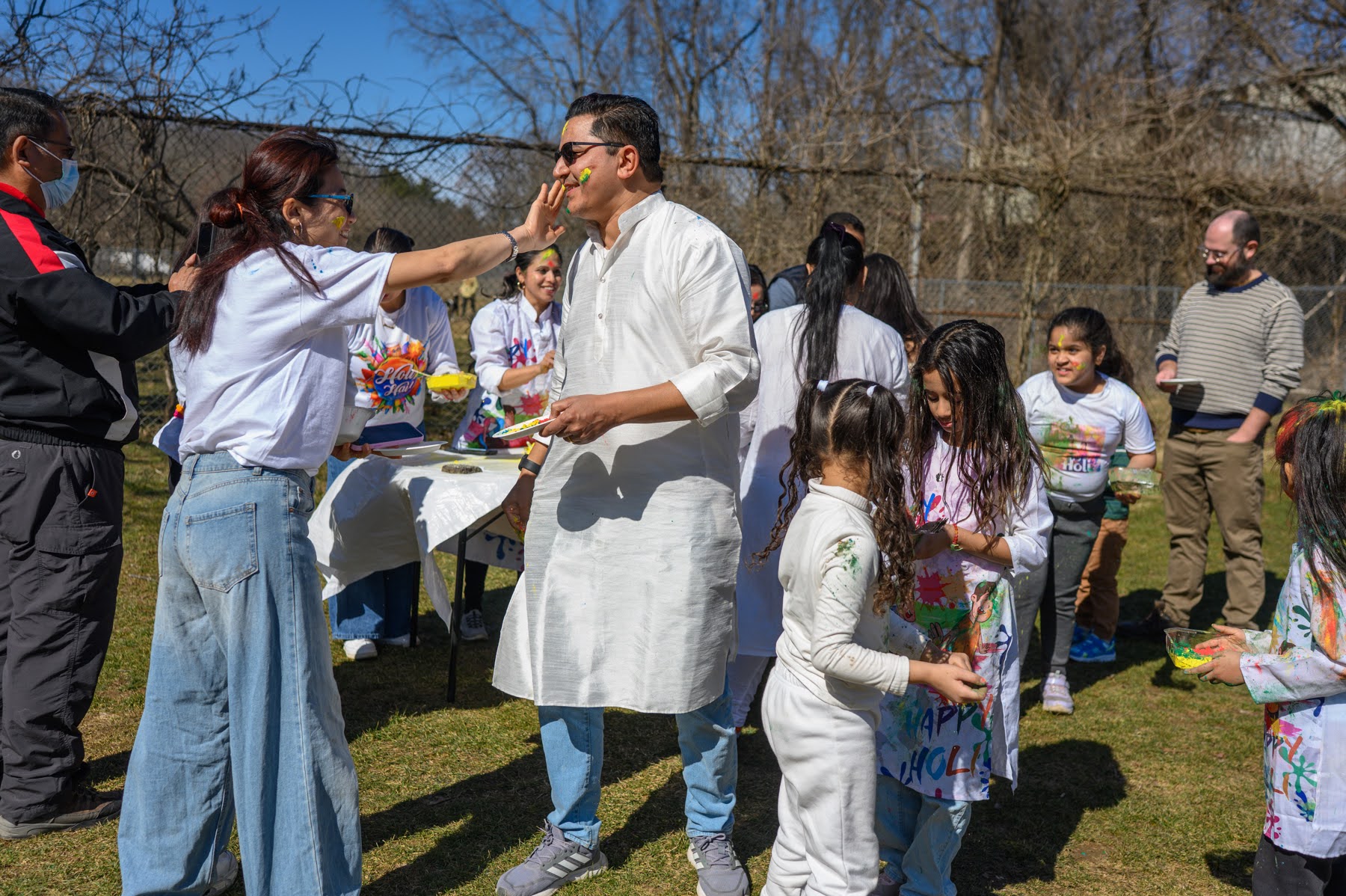 A group of people outdoors celebrate Holi by applying colored powder to each other's faces and clothes.