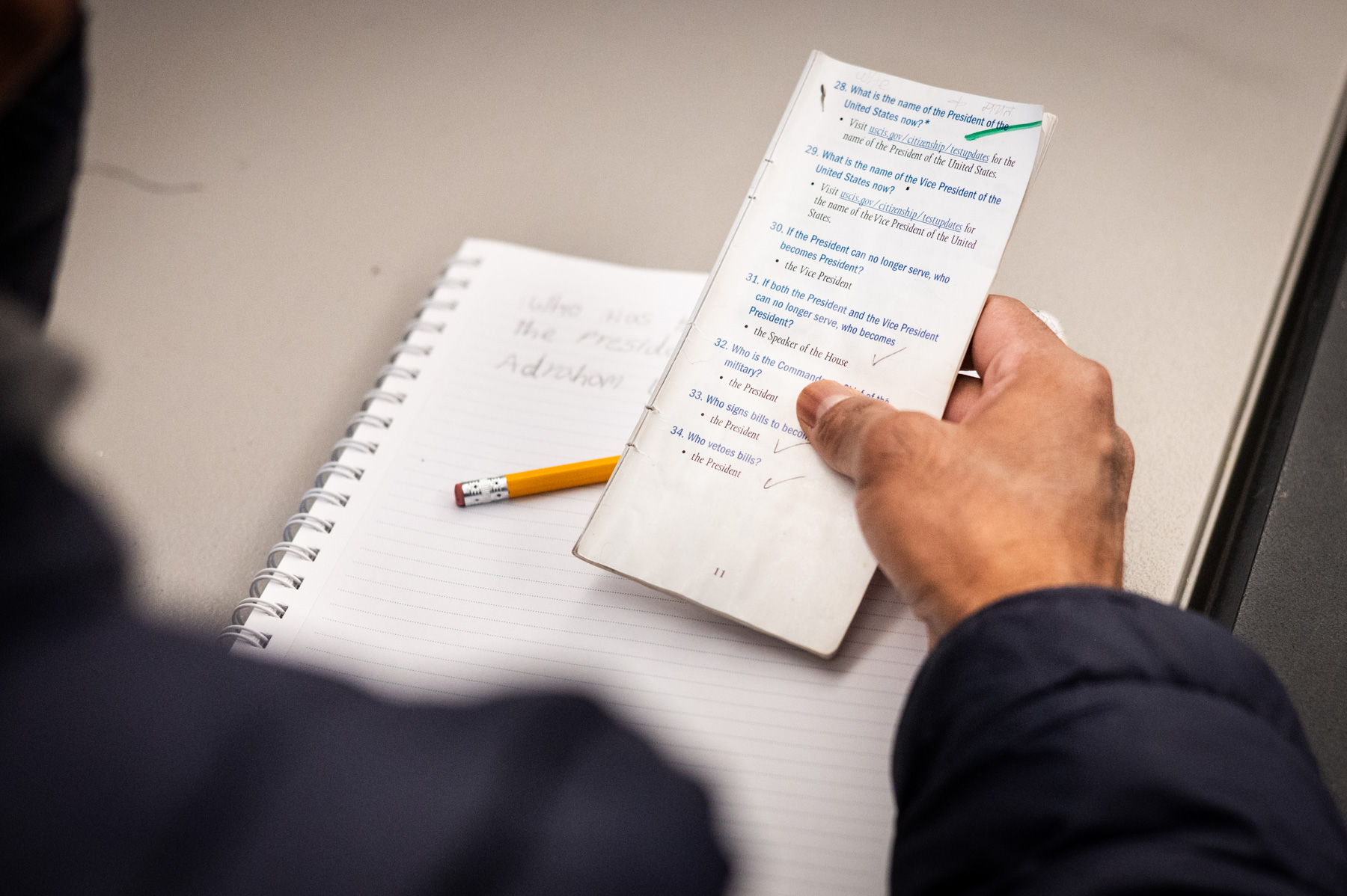 A person holding a folded checklist with handwritten notes, next to an open notebook and a pencil on a desk.