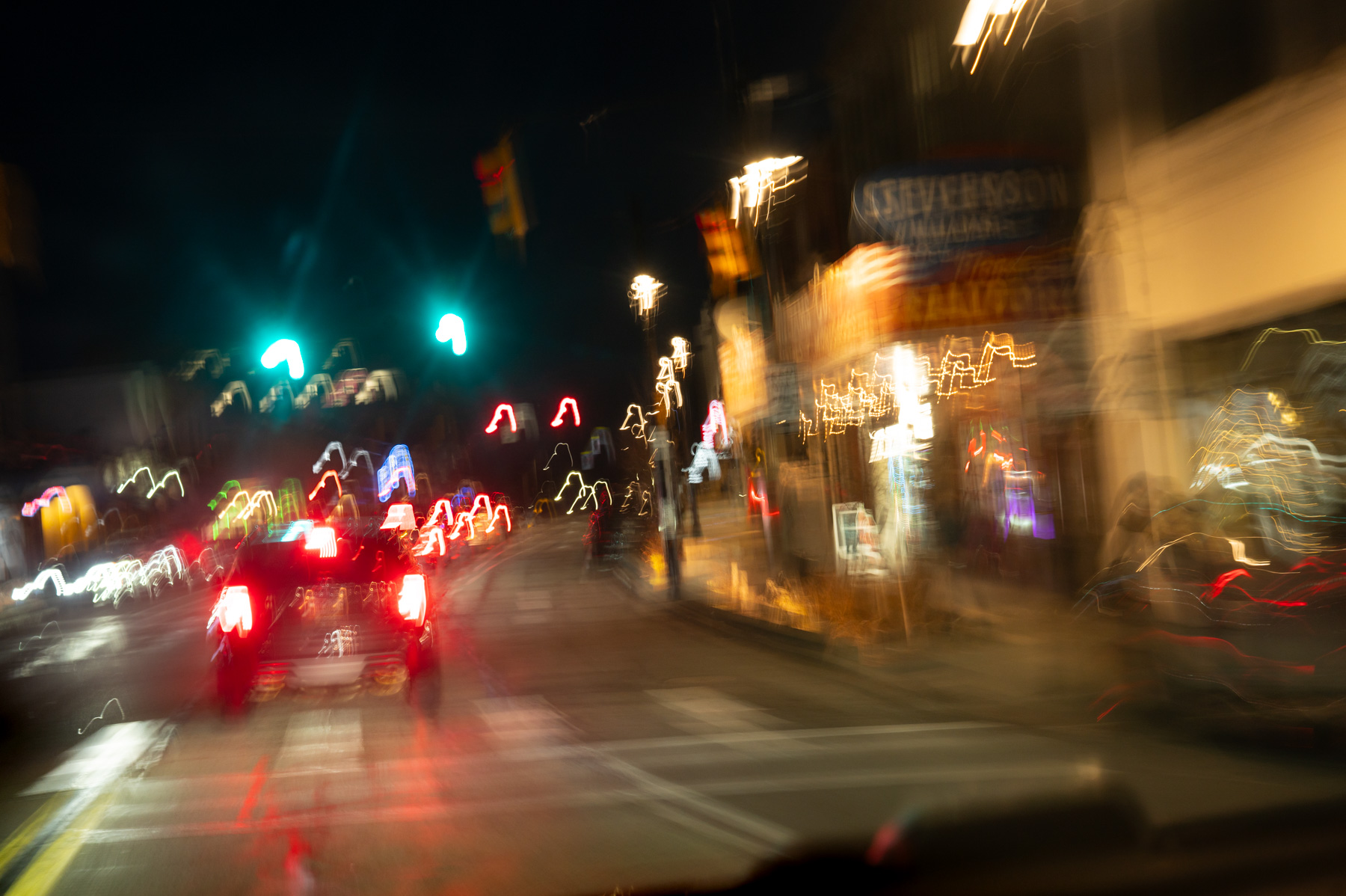 Blurred nighttime street scene with car tail lights and traffic signals, city lights streaked due to camera motion.