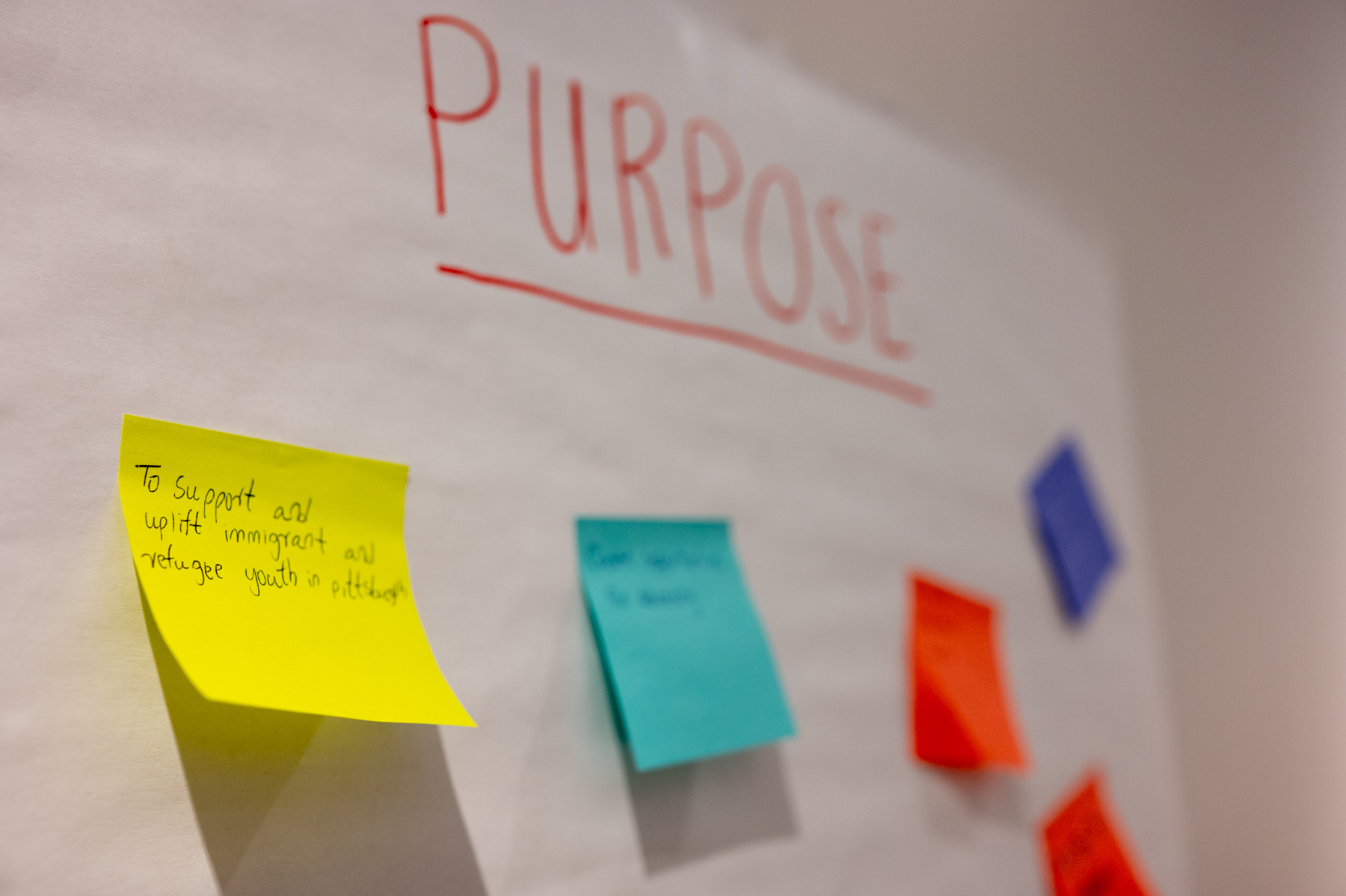 Sticky notes in red, teal, orange and purple posted on a large, white board. The word "Purpose" is written in red Sharpie on the board above the notes.  