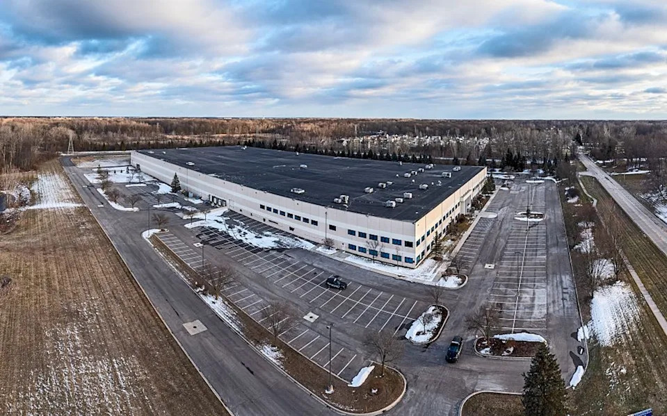 A large warehouse stands in a rural area with snow on the ground.