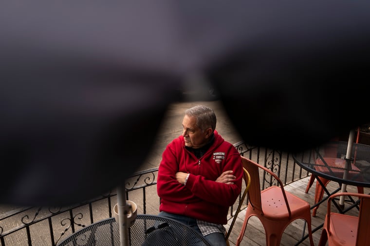 District Attorney Larry Krasner sits with a cup of coffee outside Gleaner’s Cafe in South Philadelphia's Italian Market in March 2024. He is wearing a sweatshirt repping Unite Here, the union that represents hotel, gaming, and food service workers in the city.
