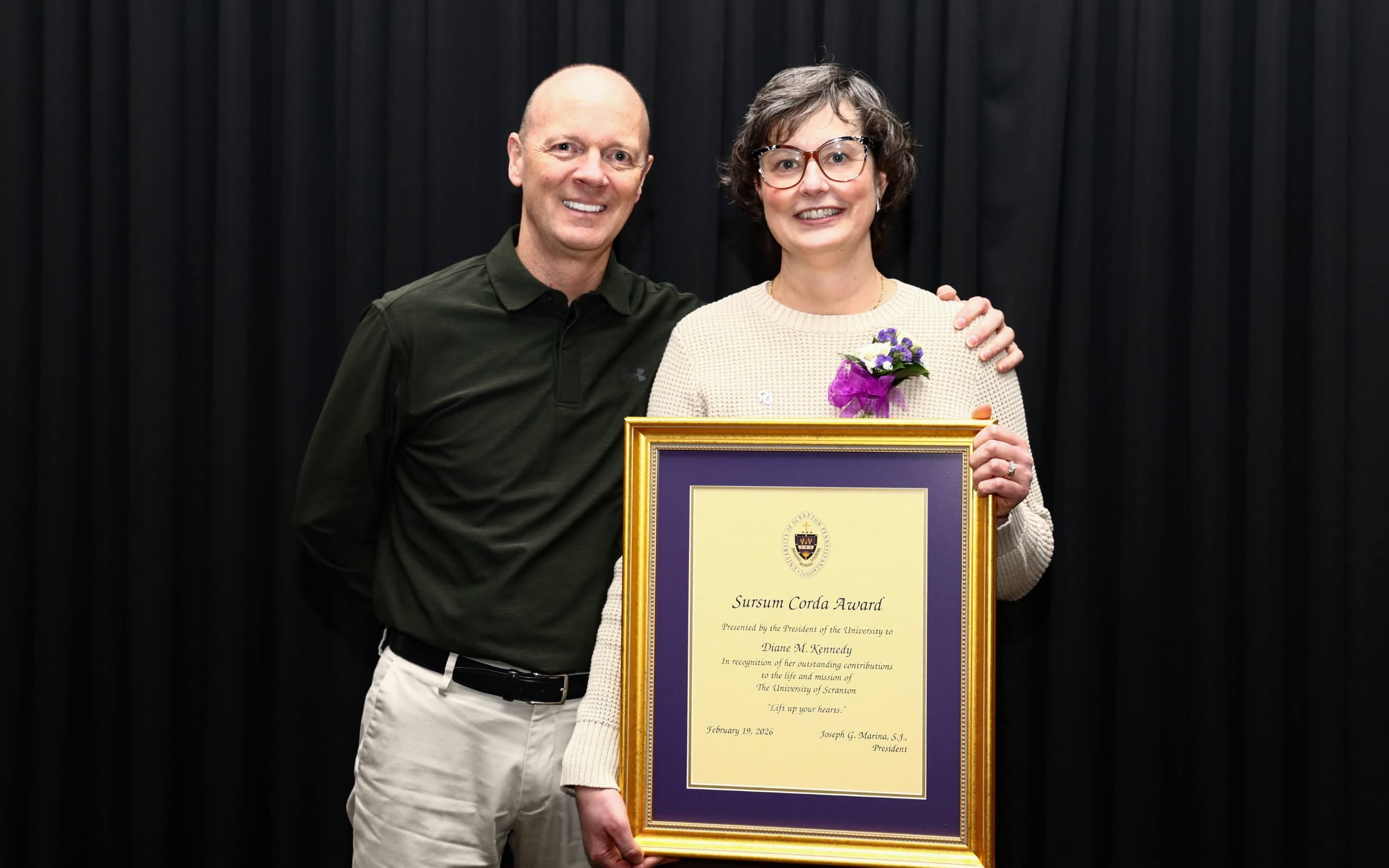 Two people pose together, one holding a framed university award certificate.