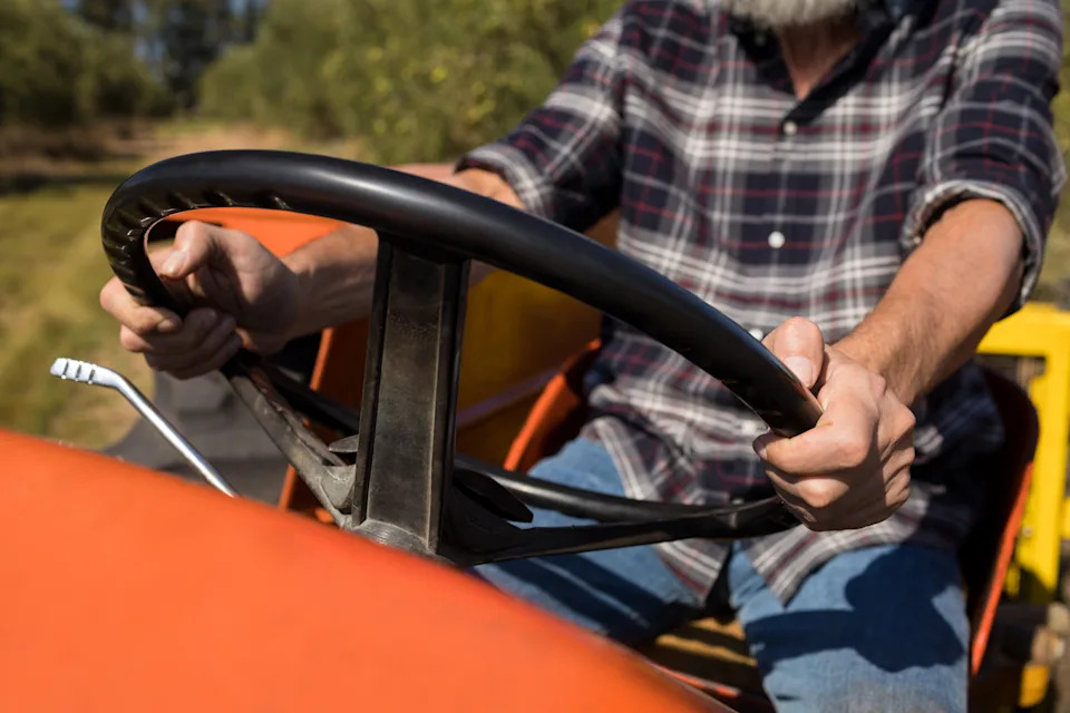 Person in plaid shirt driving a tractor, gripping the steering wheel with both hands