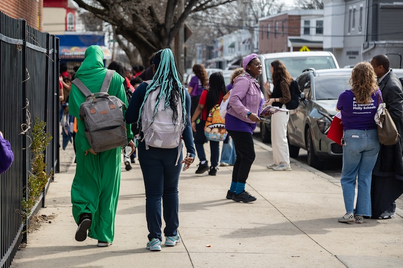 A photograph of students walking down the sidewalk on a sunny day.
