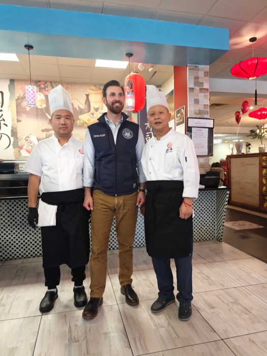 A man with a beard stands between two men in chef clothes