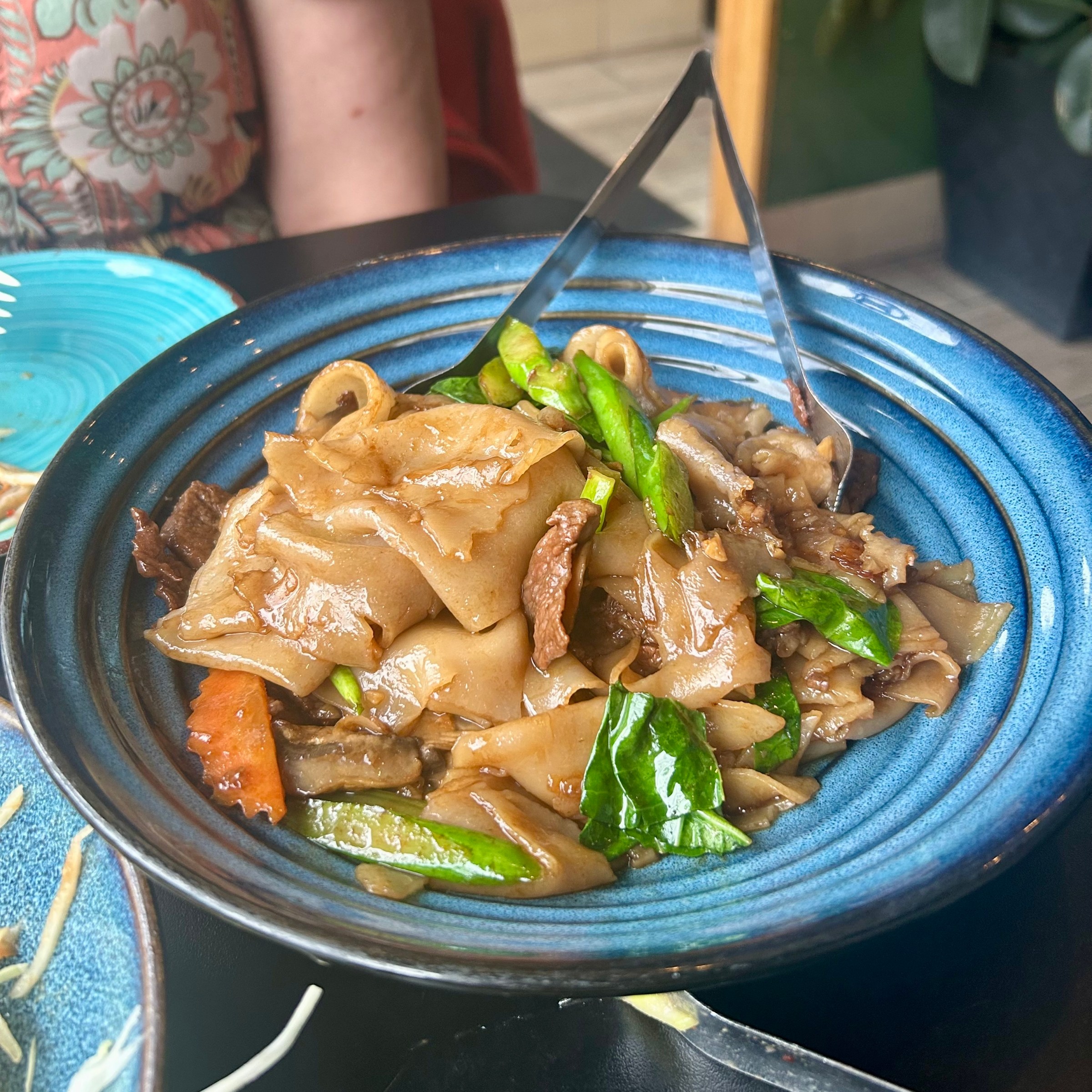 Stir-fried wide noodles with vegetables and beef in a blue bowl.