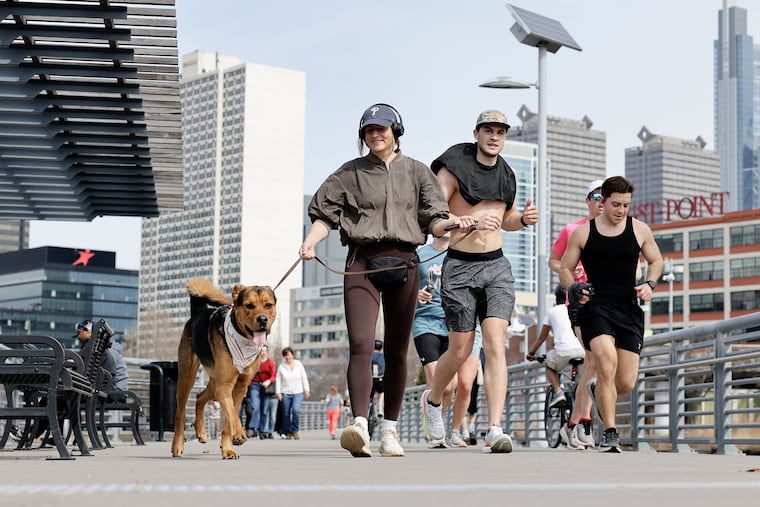 Runners and a dog walker move along the Schuylkill Banks Boardwalk earlier this month. It's been quite the month for a change of seasons.