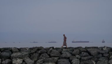 FILE - A man walks along the shore as oil tankers and cargo ships line up in the Strait of Hormuz, as seen from Khor Fakkan, United Arab Emirates, Wednesday, March 11, 2026. (AP Photo/Altaf Qadri, file)