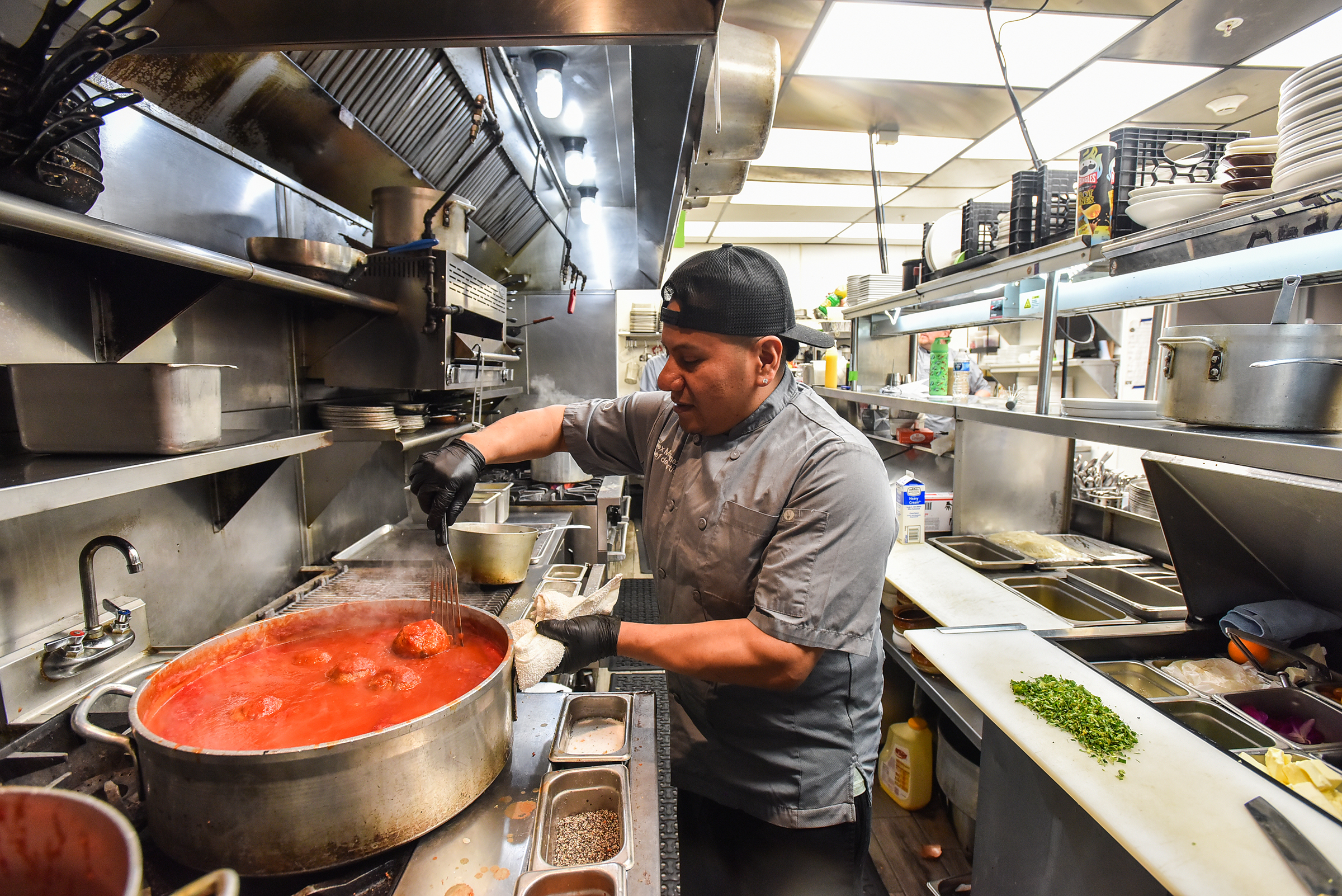 Line cook Alex Martinez stirs meatballs in the kitchen of...