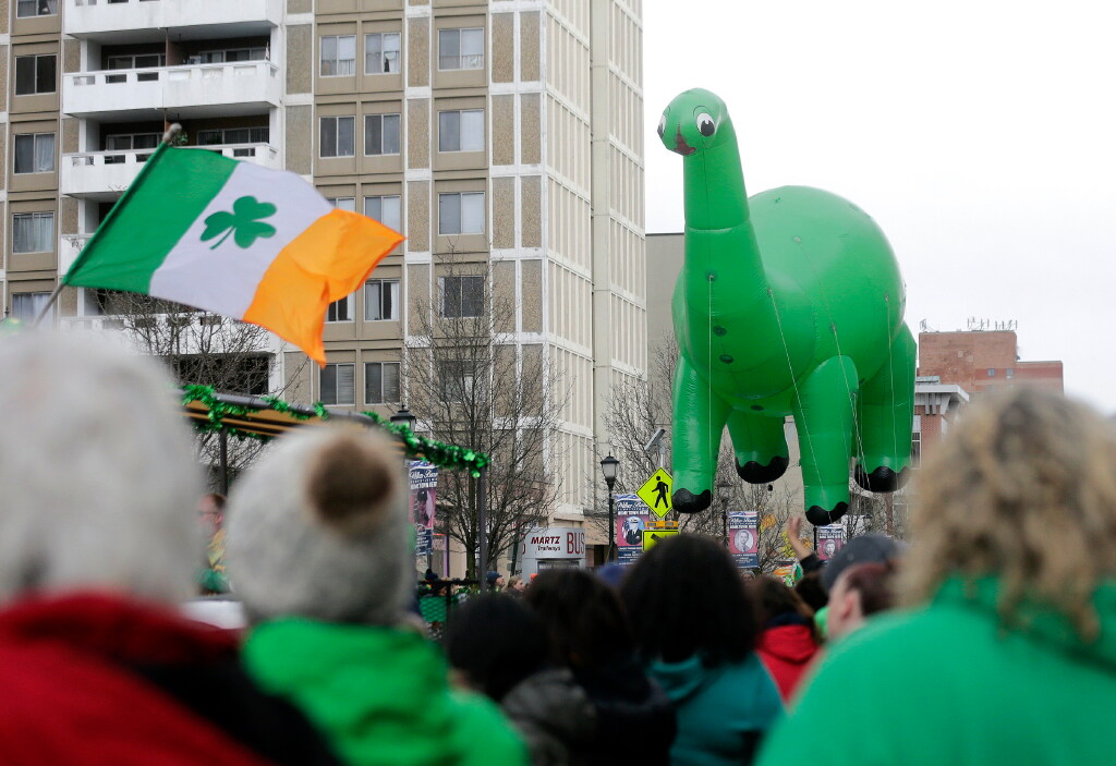 Parade goers watch as a giant inflatable dinosaur moves along...