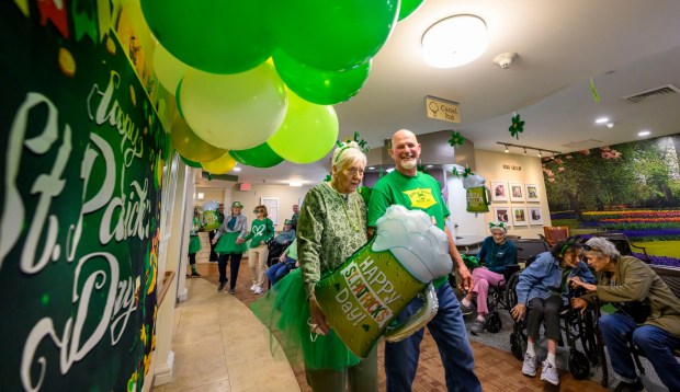 Volunteer Bob Brooks walks with Pat, a resident at Arden Courts Old Orchard memory care community in Bethlehem Township, during a St. Patrick's Day celebration Tuesday, March 17, 2026 at Arden Courts. (April Gamiz/The Morning Call)