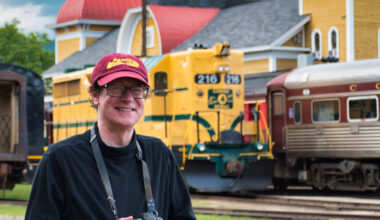 Man holding camera with yellow train in background. Solomon to lead Railroad Museum of Pennsylvania photo session.