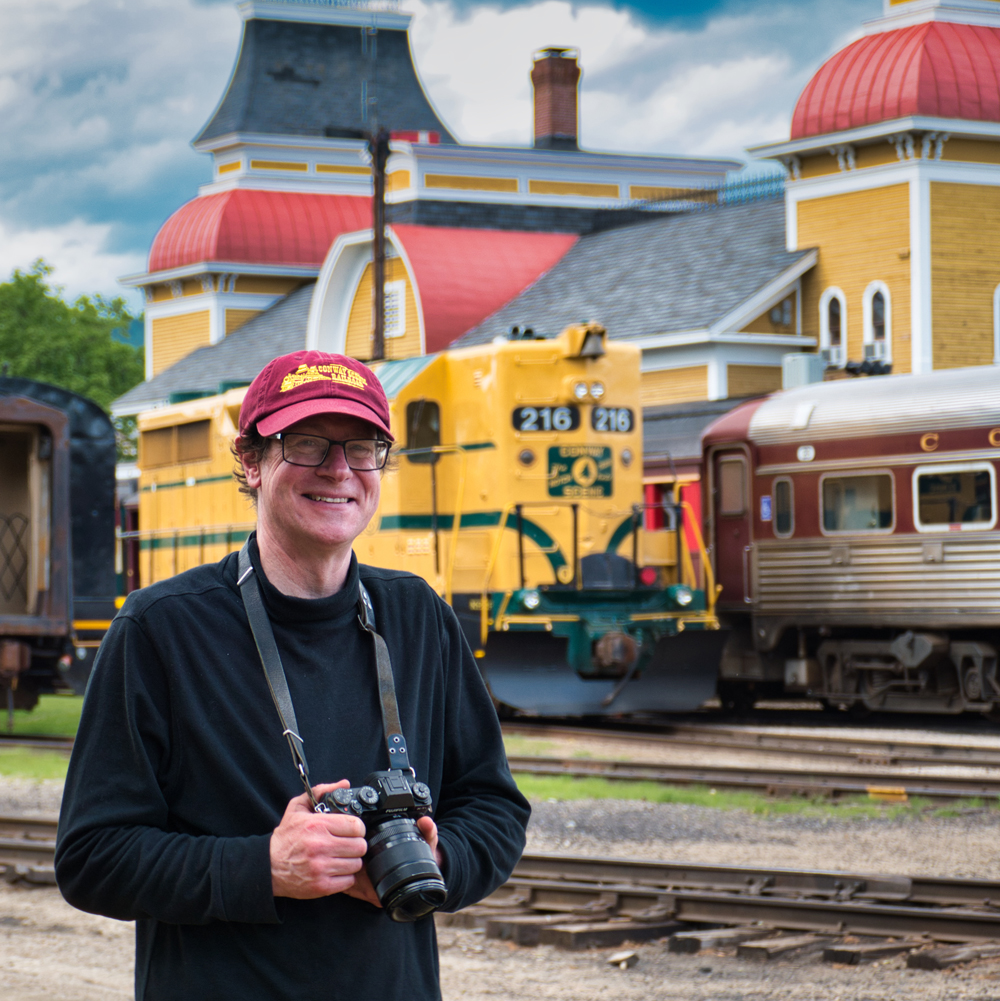 Man holding camera with yellow train in background. Solomon to lead Railroad Museum of Pennsylvania photo session.