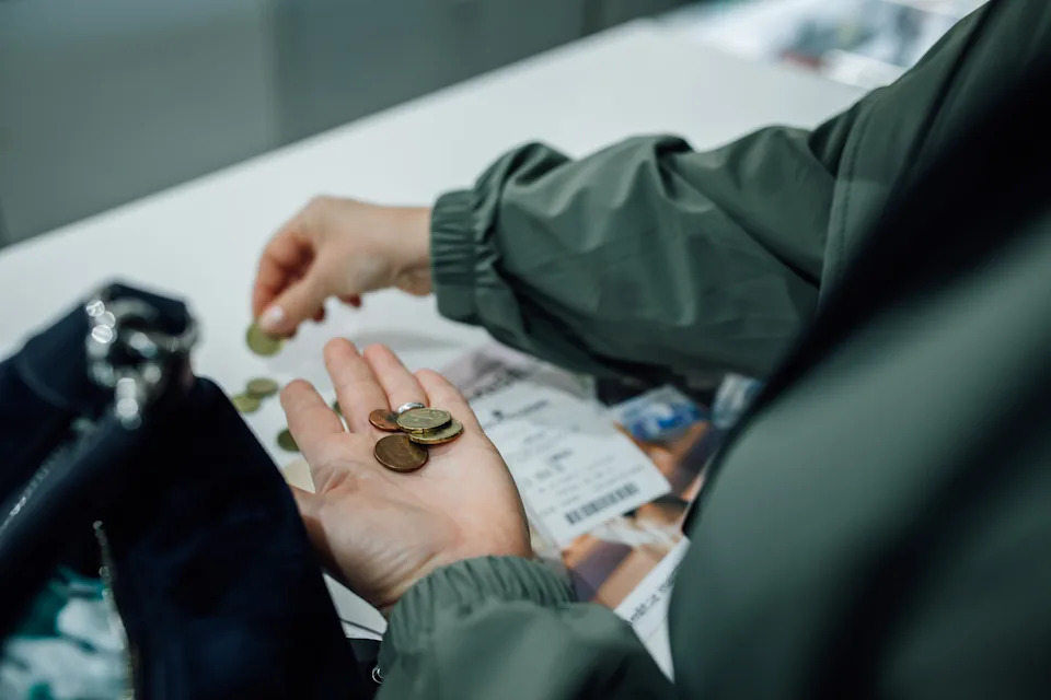 Person in jacket counting coins next to an open handbag, with a receipt visible on the table