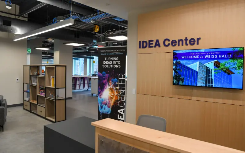 Reception area of an IDEA Center with a front desk, shelving, and a wall-mounted welcome screen.