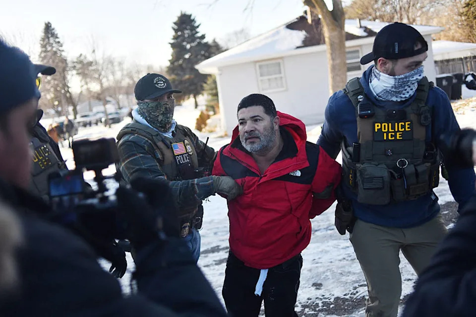 A man in a red coat is carried away by two men wearing bulletproof vests.