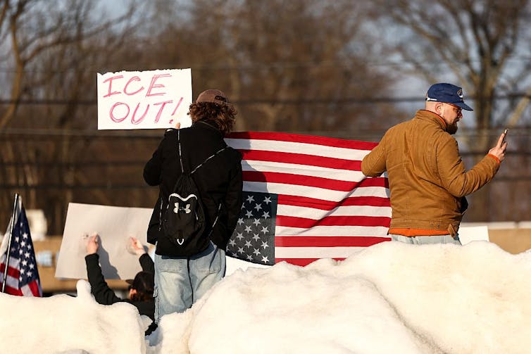 Two protestors hold an American flag upside down while protesting ICE outside.