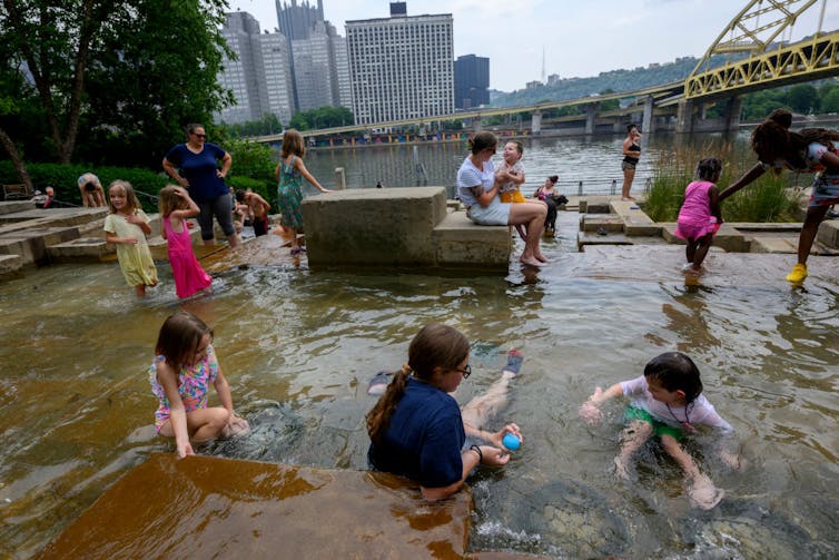 Children playing in water along a riverfront park in Pittsburgh.