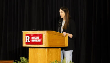 Author Liz Moore stands behind Rutgers podium and speaks to audience in front of a black backdrop.
