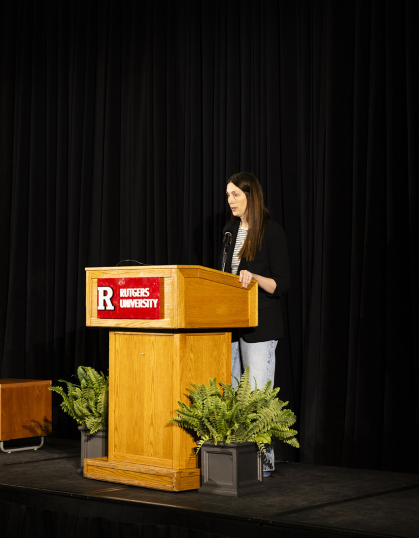 Author Liz Moore stands behind Rutgers podium and speaks to audience in front of a black backdrop.
