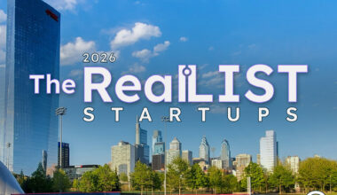 A city skyline with skyscrapers rises behind a softball field. Text in the sky reads "2026 The RealLIST STARTUPS" with a logo in the lower right corner.