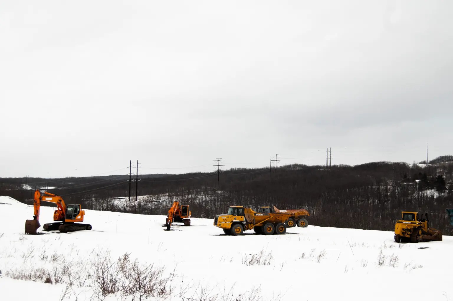 Yellow construction trucks sit in the snow near a power line.