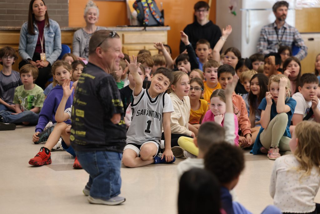 person surrounded by students raising their hands