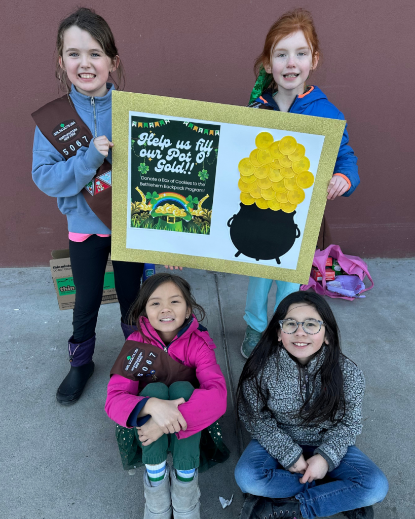 four Girl Scouts pose for photo, two holding a sign