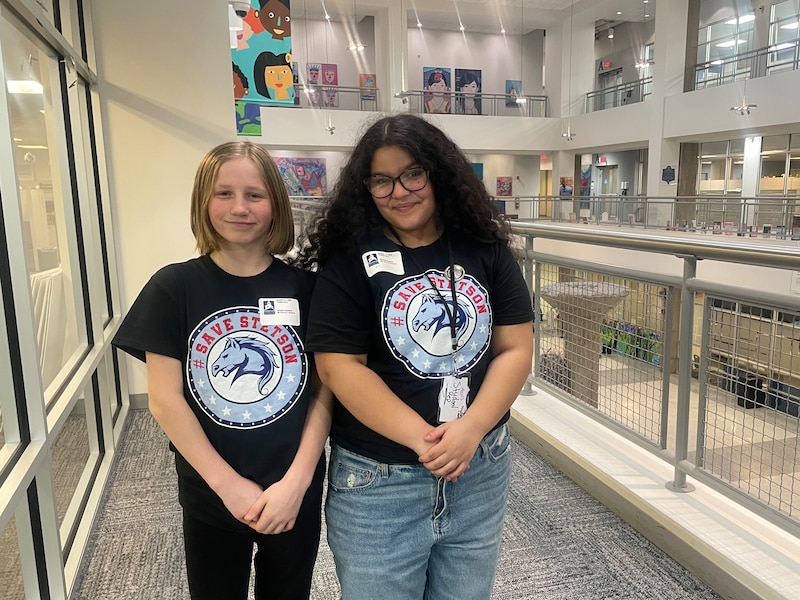A photograph of two middle school students posing for a photograph in a hallway.