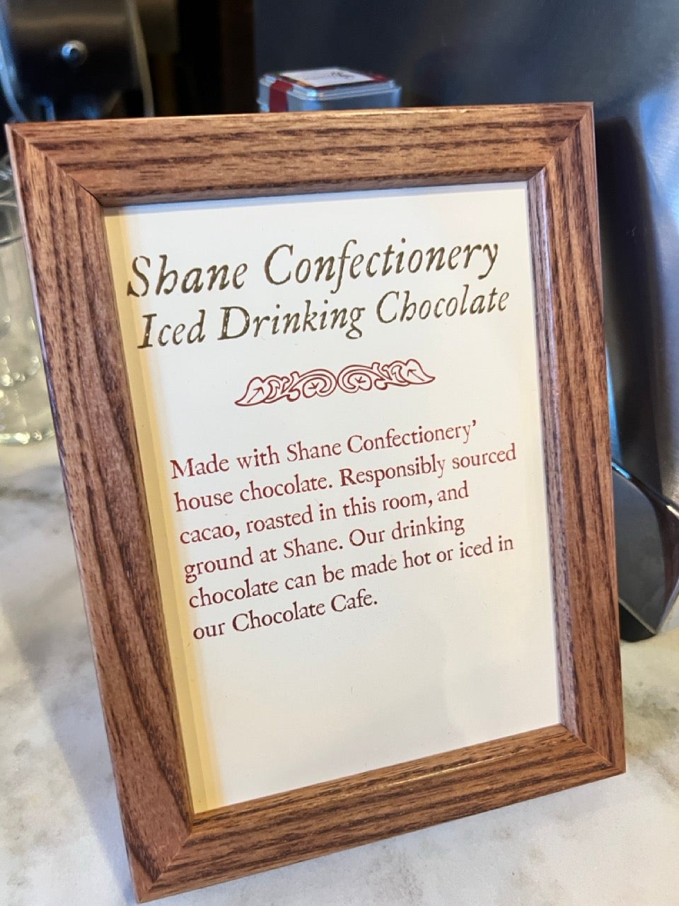 A framed sign describing the Iced Drinking Chocolate add-on option at The Cacoa Pod event space.
