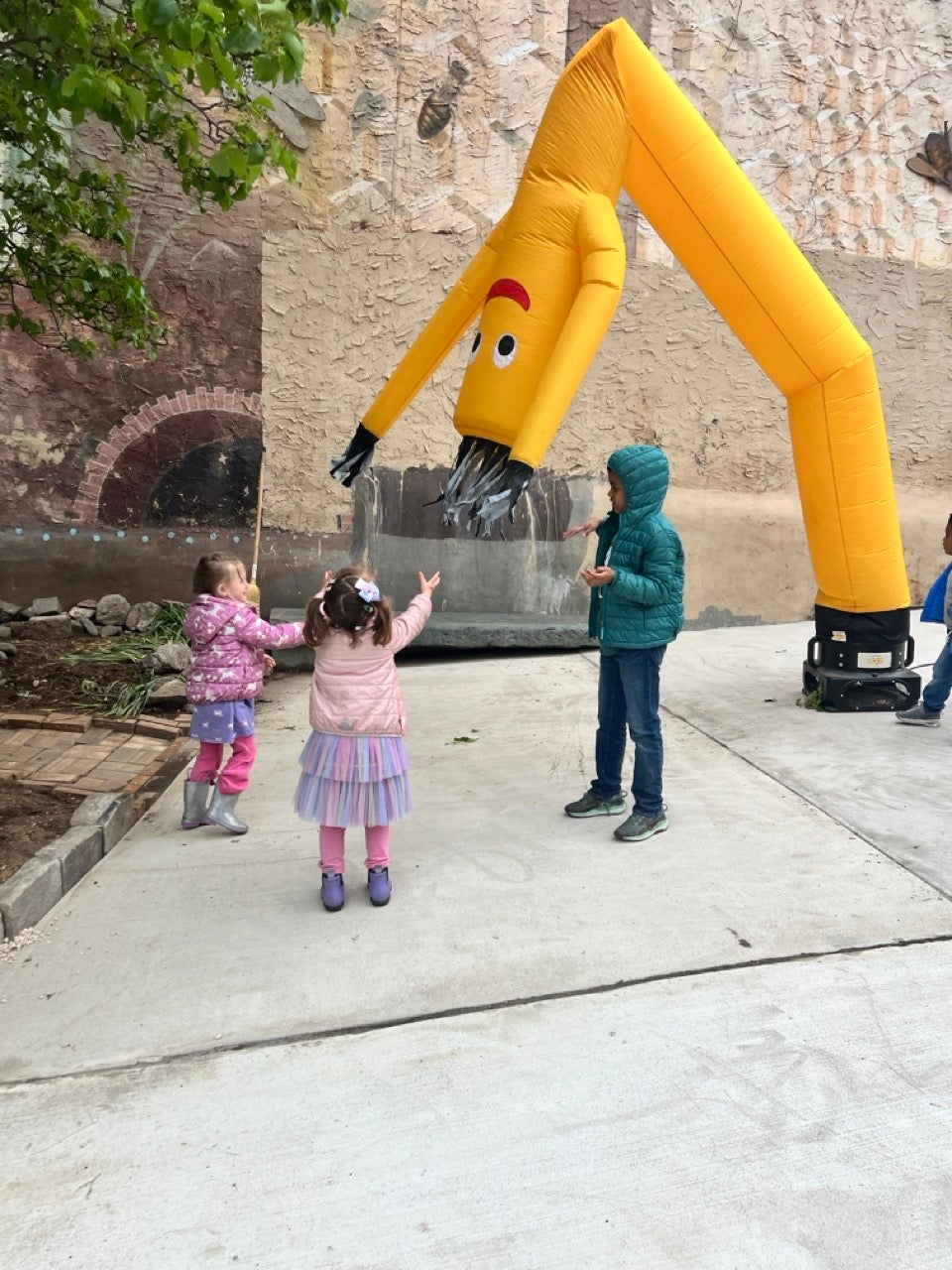 A yellow sky dancer or whatever they're called, those air powered tall skinny figures that kids love to see and businesses use to draw attention to their business. Three kids play around it.
