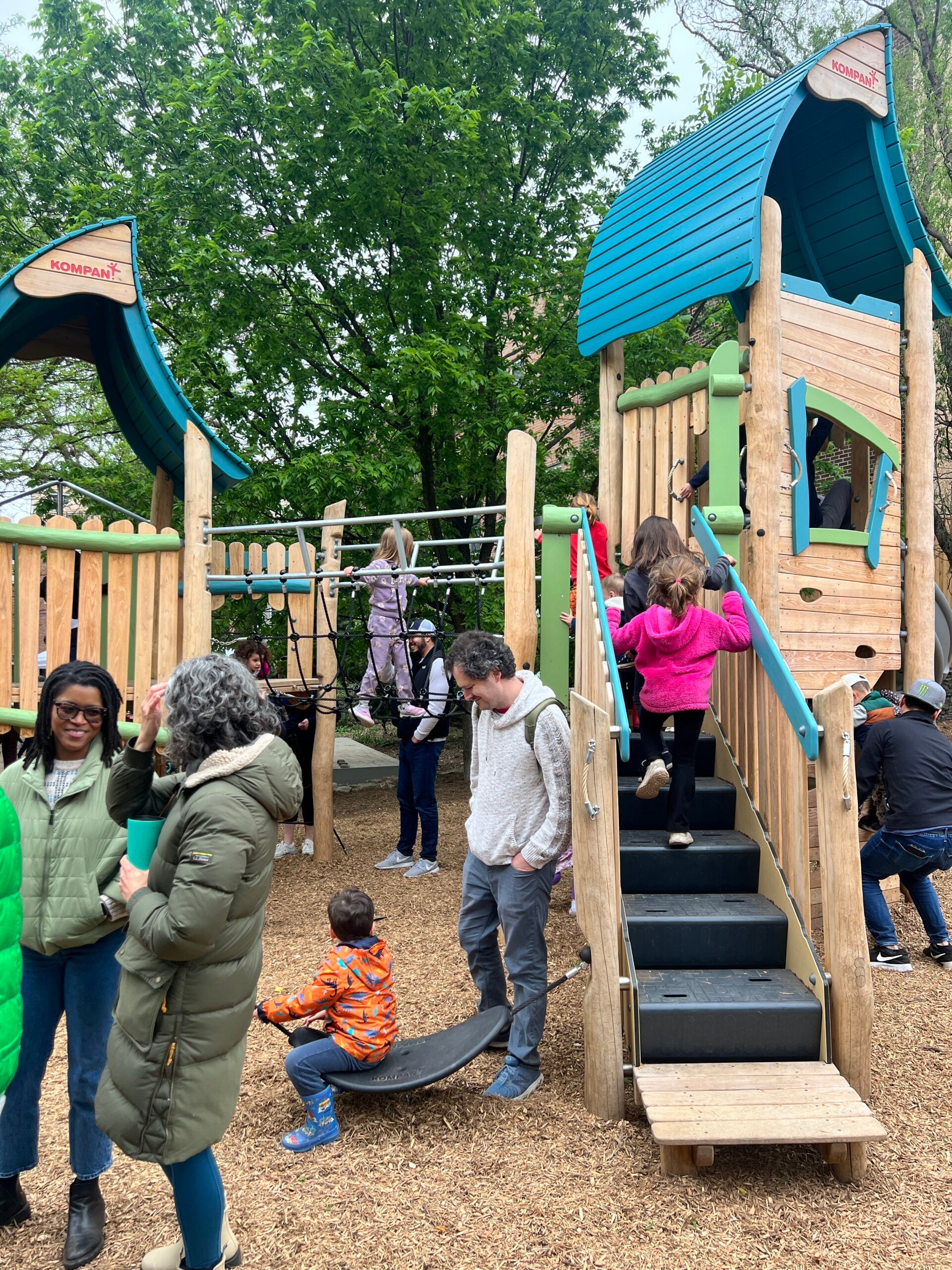 A photo of one of the big wooden structures with a bridge to cross at the new Liberty Lands Playground. Lots of kids and parents play at the opening.