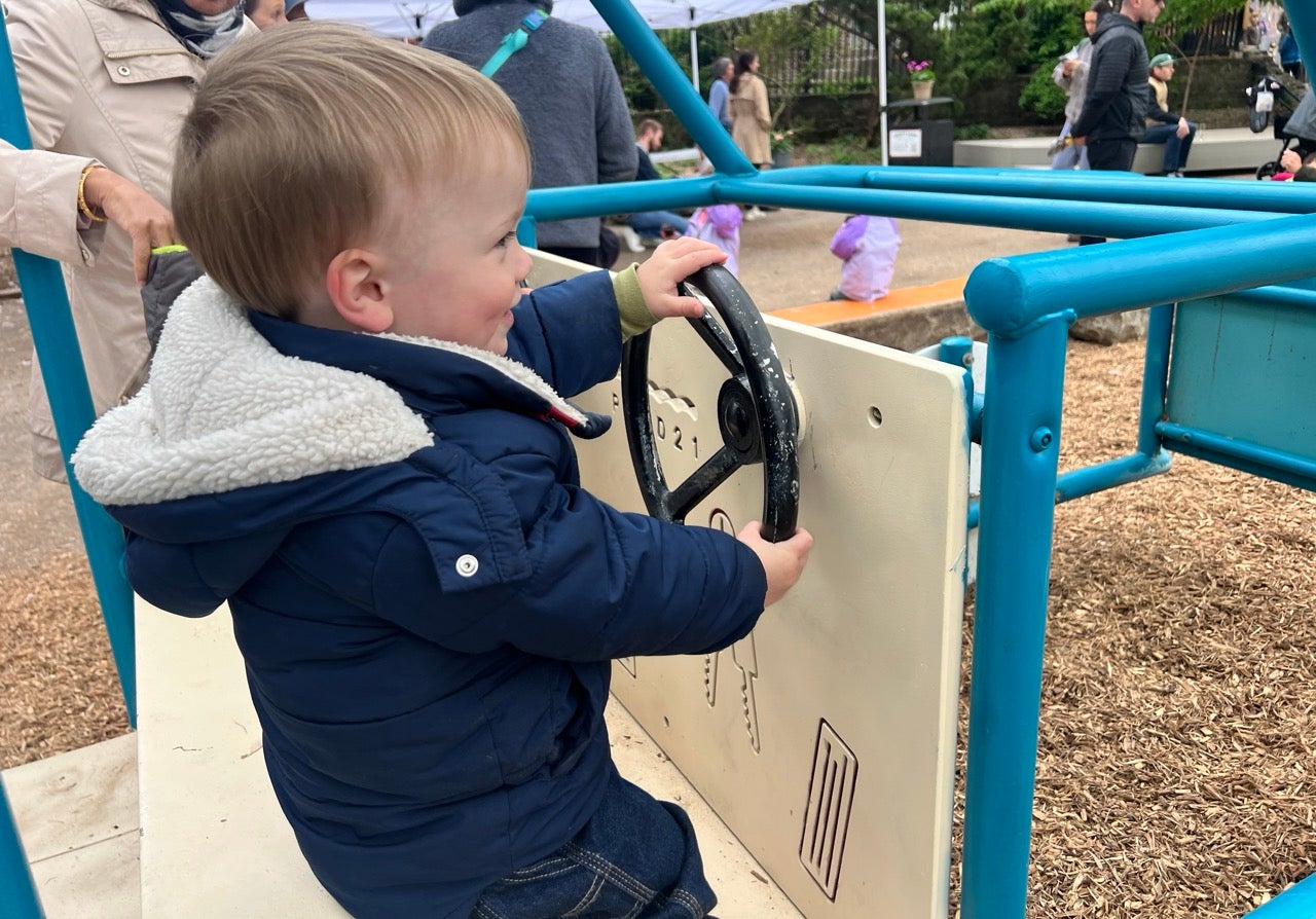A little boy pretends to drive a car holding a steering wheel on a playground "car".