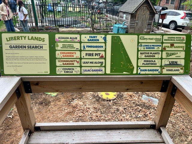 A large horizontal sign with a painted green mural about Liberty Lands Playground.