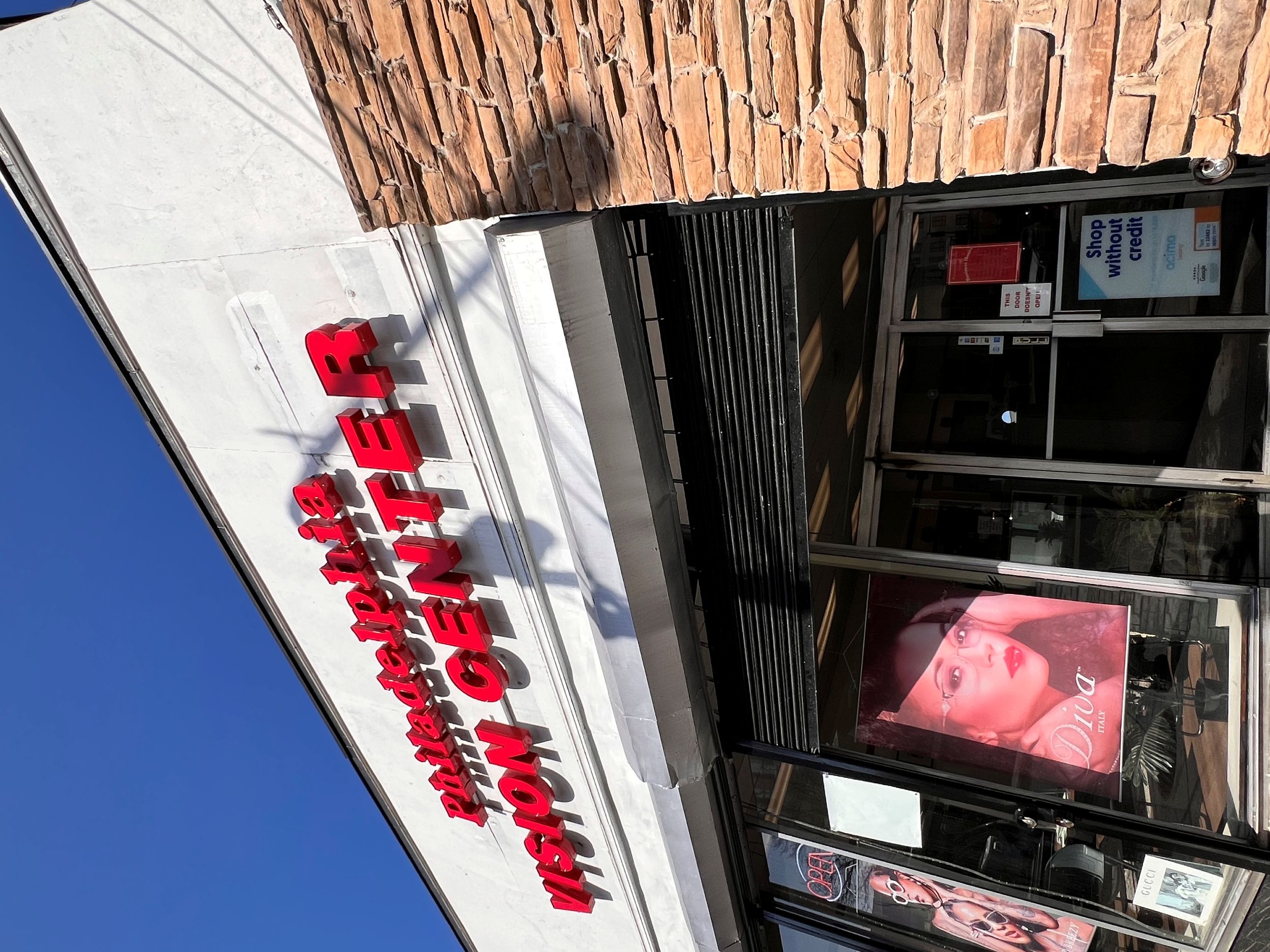 The exterior of Philadelphia Vision Center with red signage, a stone wall section, and large posters of eyeglasses in the windows.