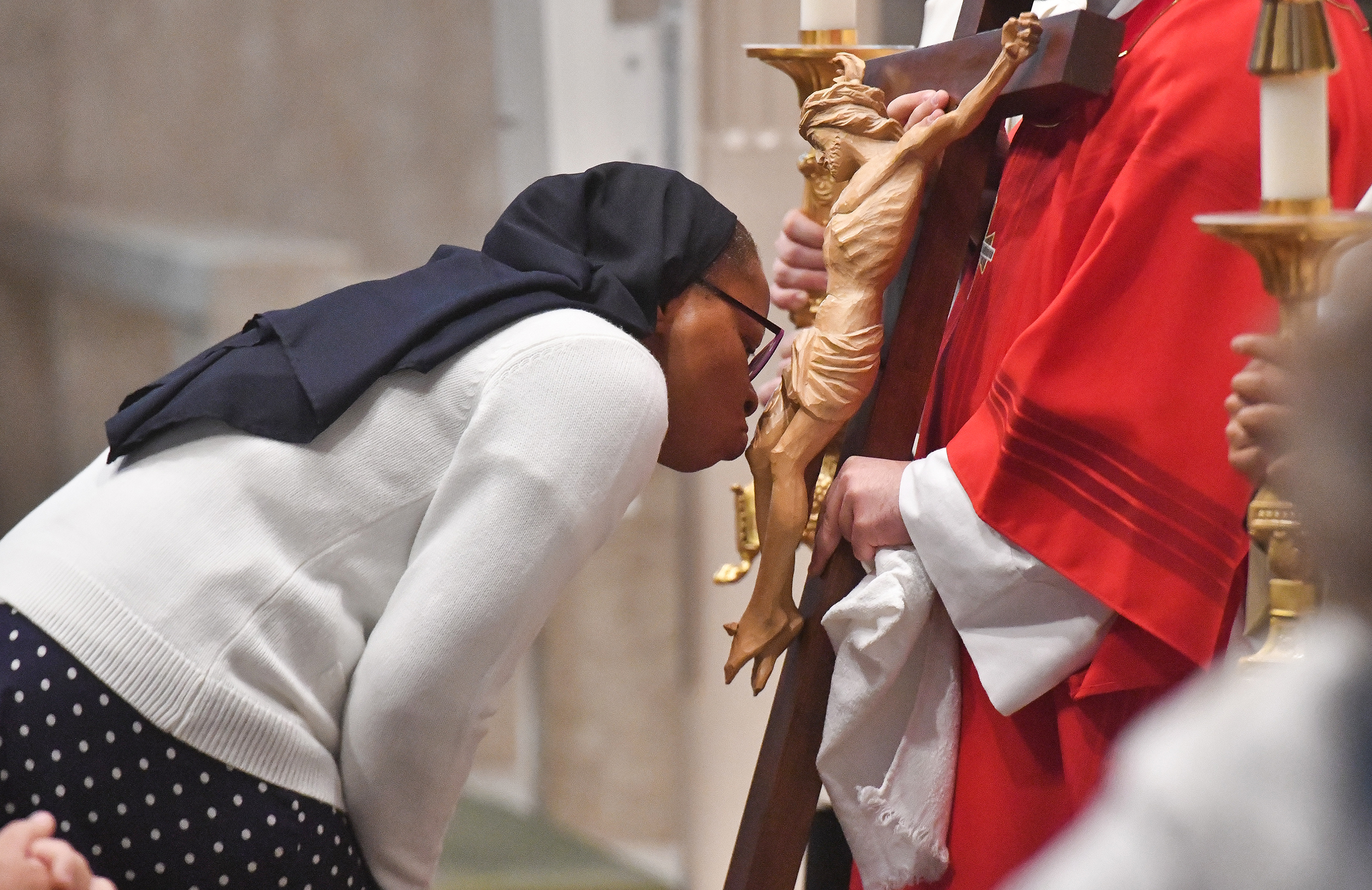 A parishioner shows adoration to the cross, held by Deacon...