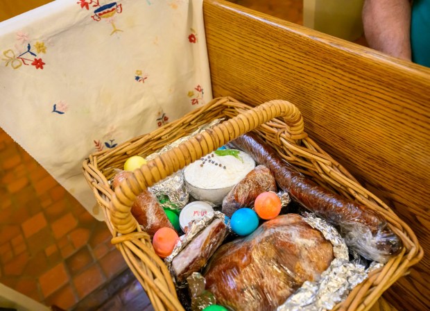 Jim Yackanicz of Bethlehem covers one of his Easter baskets by a cloth that was embroidered by his great-great grandmother Saturday, April 4, 2026, during a blessing of the food baskets on Holy Saturday at St. Anne Catholic Church in Bethlehem. (April Gamiz/The Morning Call)