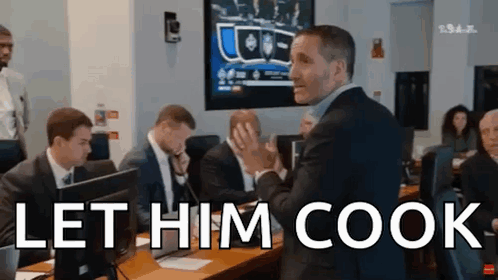a man in a suit stands in front of a group of people and says let him cook ..