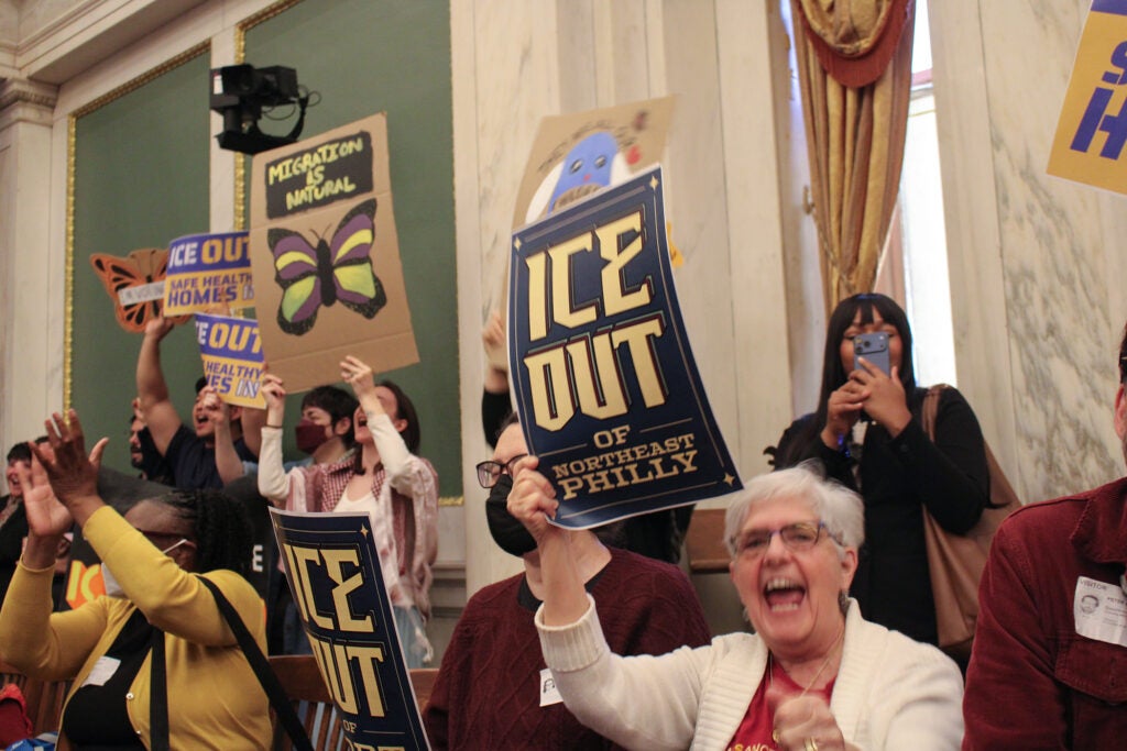 Activists hold up signs in council chambers that say 'ICE Out'