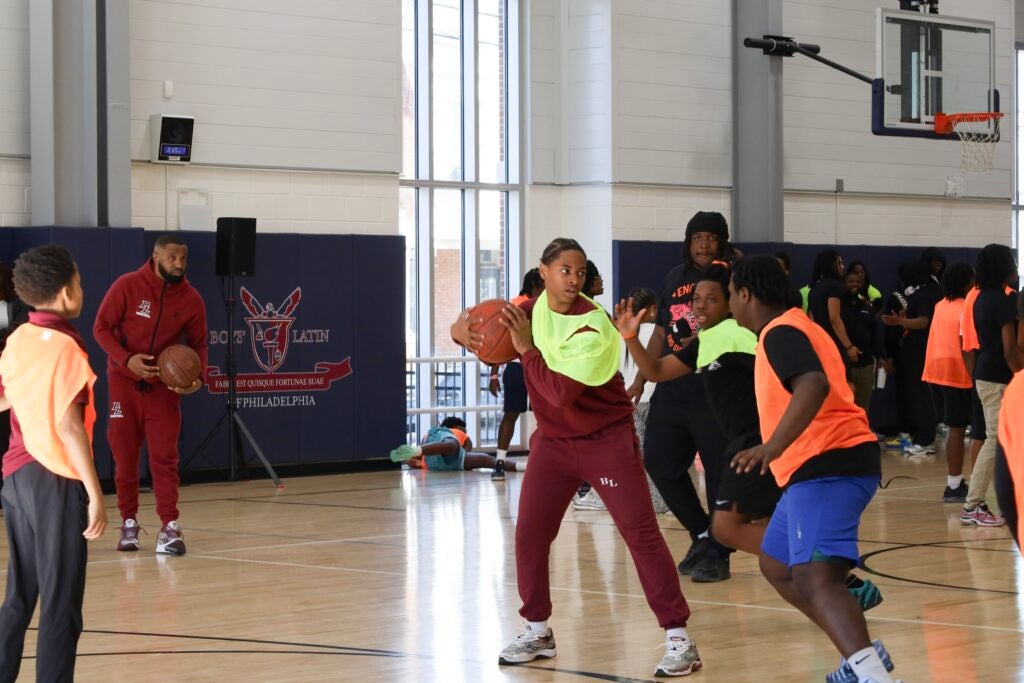A student wearing an orange jersey is defending another with the ball wearing a yellow jersey.