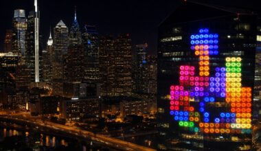 Colorful Tetris blocks are displayed in lights on a glass building at night, overlooking a city skyline with illuminated skyscrapers.